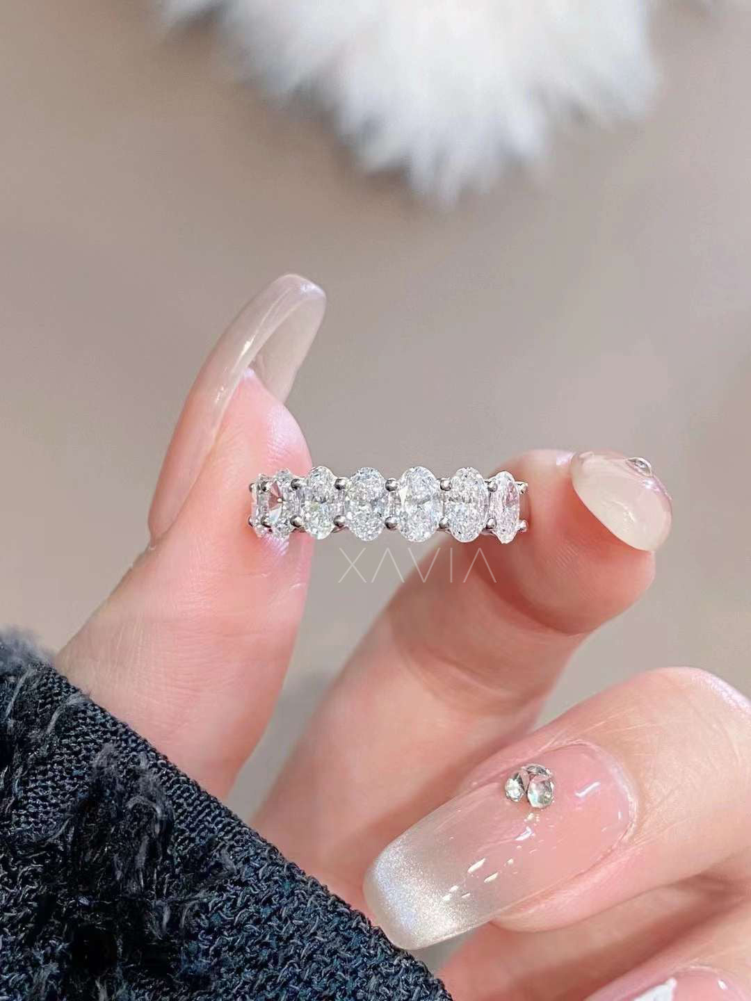 Close-up of oval lab diamond half eternity ring held between fingers